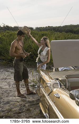 Stock Photography - View of a young couple standing by antique convertible car. Fotosearch