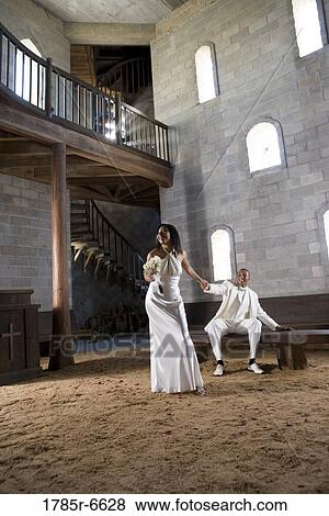Stock Photo - View of bride and groom in white holding hands inside a medieval castle. Fotosearch