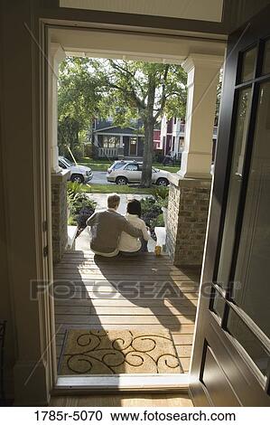 Stock Image - View of interracial couple sitting on front steps of house. Fotosearch