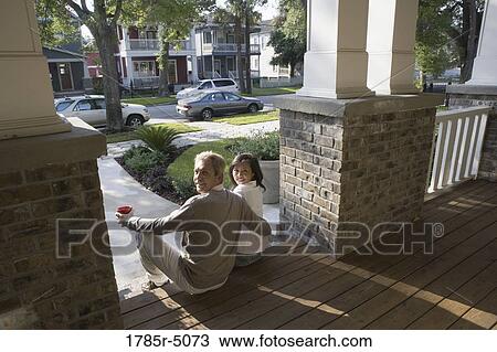 Stock Image - View of interracial couple sitting on front steps of house. Fotosearch