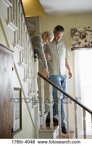 Stock Photo - View of man helping feeble senior man walk downstairs. Fotosearch