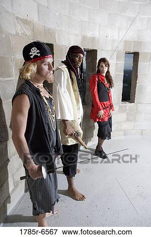 Stock Photo - View of pirates armed with a gun and a sword standing against a castle wall. Fotosearch
