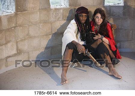 Picture - View of pirates armed with a gun hiding against a castle wall. Fotosearch