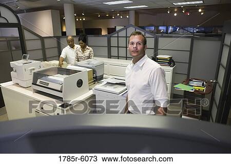 Stock Image - View over an cubicle wall of office workers by copy machines. Fotosearch