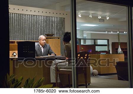 Stock Image - View through window of man and woman talking in an office. Fotosearch