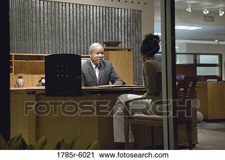 Stock Image - View through window of man and woman talking in an office. Fotosearch