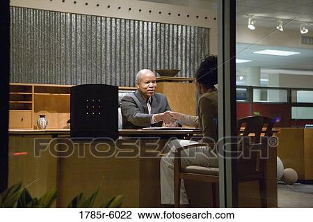 Stock Image - View through window of man and woman talking in an office. Fotosearch