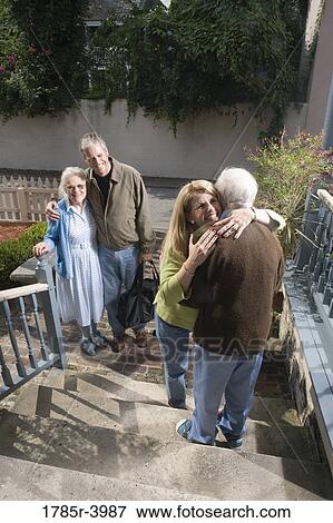 Woman cheerfully hugging senior man on steps while man and senior woman watch View Large Photo Image Stock Photo - Woman cheerfully hugging senior man on steps while man and senior woman watch. Fotosearch
