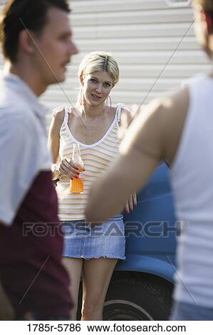 Stock Photograph - Woman drinking an orange soda, watching two men talking in foreground. Fotosearch