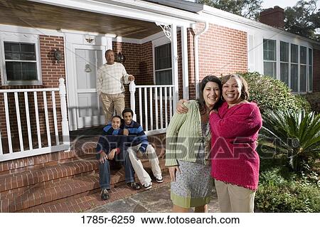 Woman embracing her daughter-in-law in front of house with family in background View Large Photo Image Stock Photo - Woman embracing her daughter-in-law in front of house with family in background. Fotosearch