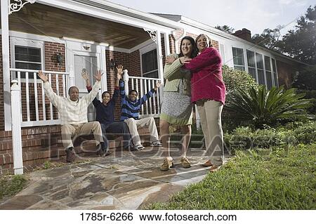 Stock Photograph - Woman embracing her daughter-in-law in front of house with family in background. Fotosearch
