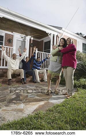 Woman embracing her daughter-in-law in front of house with family in background View Large Photo Image Stock Photography - Woman embracing her daughter-in-law in front of house with family in background. Fotosearch
