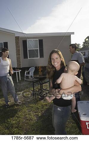 Stock Photo - Woman holding baby in backyard, grill in background. Fotosearch