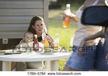 Woman holding baby sitting at picnic table View Large Photo Image Picture - Woman holding baby sitting at picnic table. Fotosearch