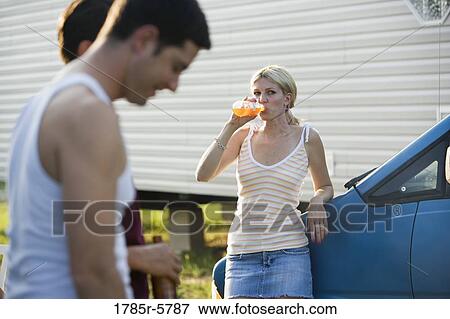 Woman leaning against van drinking an orange soda, watching two men talking in foreground View Large Photo Image Stock Photo - Woman leaning against van drinking an orange soda, watching two men talking in foreground. Fotosearch