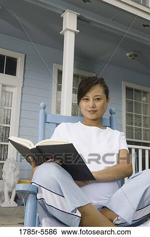 Young Asian woman sitting on a rocking chair reading a book in front of house View Large Photo Image Stock Photograph - Young Asian woman sitting on a rocking chair reading a book in front of house. Fotosearch
