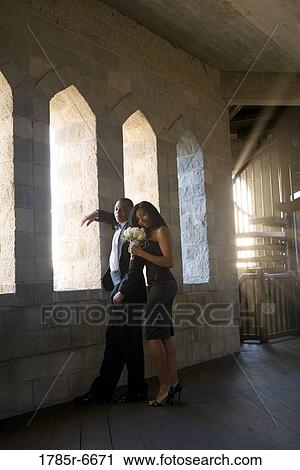 Stock Image - Young couple in formal attire looking out window of medieval castle. Fotosearch