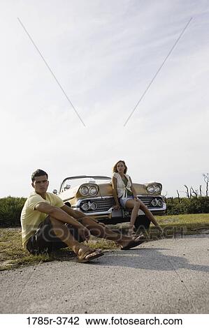 Young couple sitting beside antique convertible car View Large Photo Image Stock Image - Young couple sitting beside antique convertible car. Fotosearch