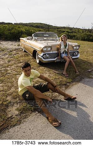 Young couple sitting beside antique convertible car View Large Photo Image Stock Image - Young couple sitting beside antique convertible car. Fotosearch