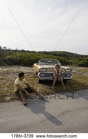 Young couple sitting beside antique convertible car View Large Photo Image Stock Photo - Young couple sitting beside antique convertible car. Fotosearch