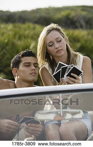 Stock Photo - Young couple sitting in antique convertible car looking at photographs. Fotosearch