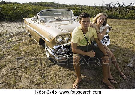 Young couple sitting on front bumper of antique convertible car View Large Photo Image Stock Photography - Young couple sitting on front bumper of antique convertible car. Fotosearch