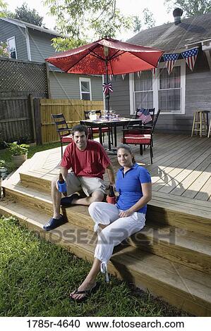 Young couple sitting on steps of their backyard patio with 4th of July decorations in background View Large Photo Image Stock Image - Young couple sitting on steps of their backyard patio with 4th of July decorations in background. Fotosearch