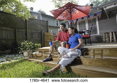Young couple sitting on steps of their backyard patio with 4th of July decorations in background View Large Photo Image Stock Image - Young couple sitting on steps of their backyard patio with 4th of July decorations in background. Fotosearch