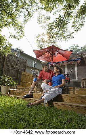 Stock Image - Young couple sitting on steps of their backyard patio with 4th of July decorations in background. Fotosearch