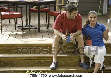 Young couple sitting on steps of their backyard patio with cold beverages View Large Photo Image Stock Image - Young couple sitting on steps of their backyard patio with cold beverages. Fotosearch