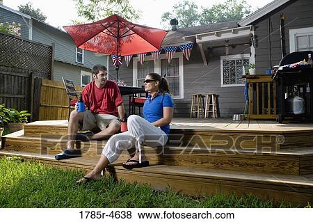 Stock Photo - Young couple sitting on steps of their backyard patio with 4th of July decorations in background. Fotosearch