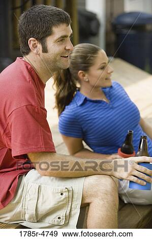 Stock Photo - Young couple sitting on steps of their backyard patio with cold beverages. Fotosearch