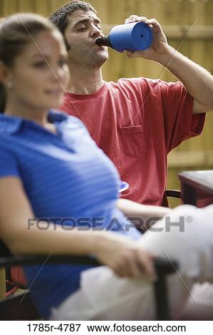 Young couple sitting together, man drinking a cold beverage View Large Photo Image Stock Photo - Young couple sitting together, man drinking a cold beverage. Fotosearch