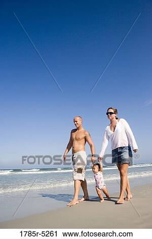 Stock Image - Young family strolling along the beach. Fotosearch