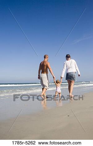Stock Image - Young family strolling along the beach. Fotosearch