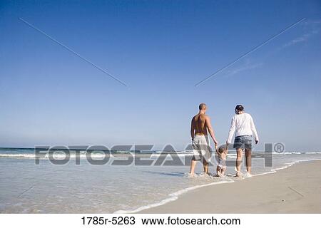 Stock Image - Young family strolling along the beach. Fotosearch
