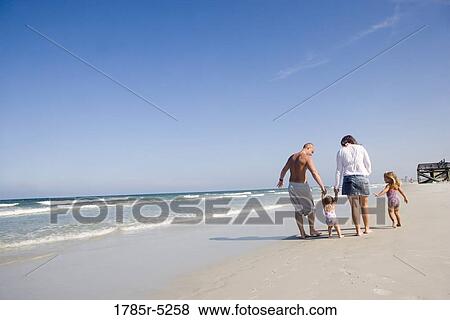 Stock Photo - Young family strolling along the beach. Fotosearch