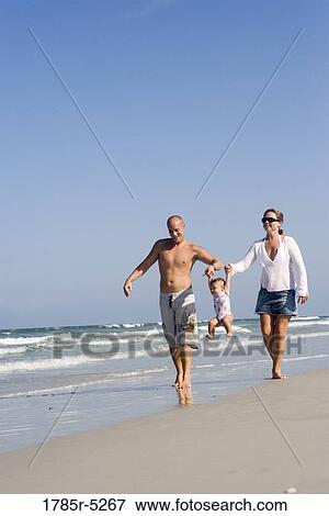 Young family strolling along the beach View Large Photo Image Stock Photo - Young family strolling along the beach. Fotosearch