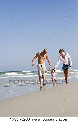 Stock Photograph - Young family strolling along the beach. Fotosearch