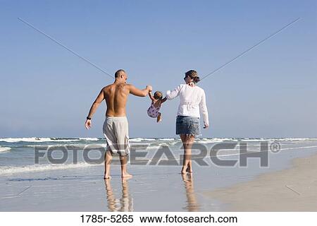 Stock Photography - Young family strolling along the beach. Fotosearch