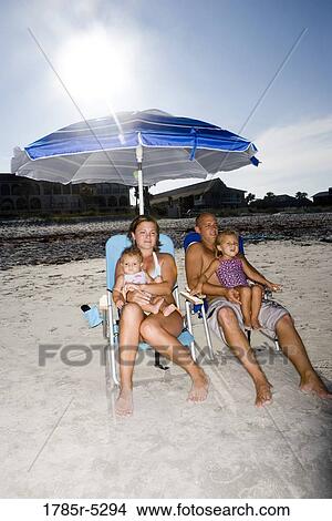 Young family with two young girls sitting on beach chairs under a beach umbrella View Large Photo Image Picture - Young family with two young girls sitting on beach chairs under a beach umbrella. Fotosearch