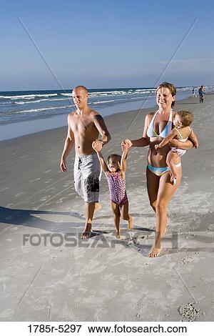 Stock Photo - Young family with young and infant daughters walking on beach while holding hands. Fotosearch