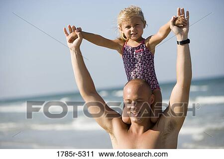 Stock Image - Young father carrying daughter on his shoulders at the beach. Fotosearch