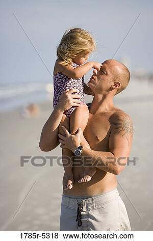 Stock Photo - Young father holding and playing with daughter at the beach. Fotosearch