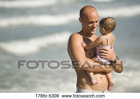 Young father holding baby daughter at the beach View Large Photo Image Stock Photo - Young father holding baby daughter at the beach. Fotosearch
