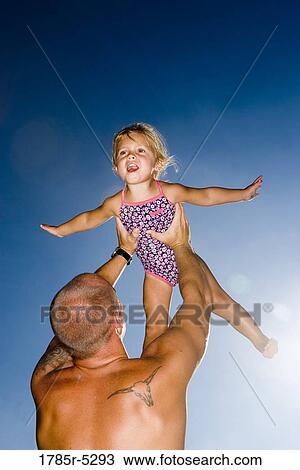 Stock Image - Young father holding daughter up in the air. Fotosearch