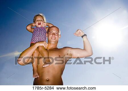 Picture - Young father holding daughter up on his shoulder while flexing his arm. Fotosearch