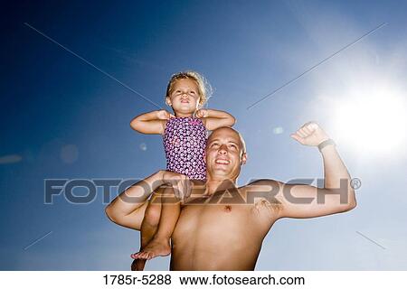 Young father holding daughter up on his shoulder while flexing his arm View Large Photo Image Stock Photo - Young father holding daughter up on his shoulder while flexing his arm. Fotosearch
