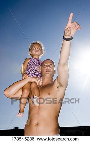Stock Photograph - Young father holding daughter up on his shoulder while pointing. Fotosearch