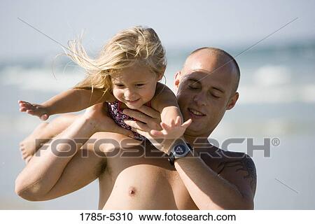 Stock Image - Young father holding his young daughter on his shoulders, while she pretends to fly. Fotosearch